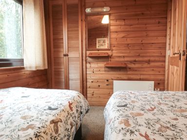 A bedroom with two beds with animal patterned bedspreads a window with curtain a wooden wardrobe a mirror and wooden walls at Sycamore Lodge in Liverton near Danby