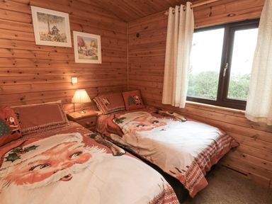 A bedroom with two single beds with santa claus bedding a lamp on a small wooden bedside table and two framed pictures on wooden walls at Sycamore Lodge in Liverton near Danby