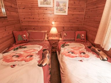 A wooden bedroom with two single beds with santa claus bedspreads and pillows a nightstand with a lamp between the beds and framed pictures on the wall at Sycamore Lodge in Liverton near Danby
