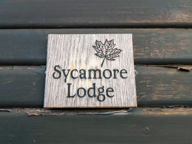 A wooden sign with a leaf and the text Sycamore Lodge on a dark wooden wall at Sycamore Lodge in Liverton near Danby