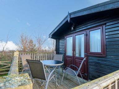 An outdoor wooden deck with a round table and four chairs outside a black wooden building at Sycamore Lodge in Liverton near Danby