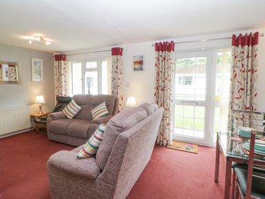 A living room with sofas a glass dining table and curtains at Sycamores Rosecraddoc Lodge near Liskeard