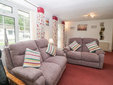 A living room with two fabric sofas with striped cushions next to windows with patterned curtains at Sycamores Rosecraddoc Lodge near Liskeard