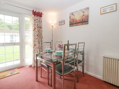 A dining area with a glass table and four chairs near a door and window at Sycamores Rosecraddoc Lodge near Liskeard