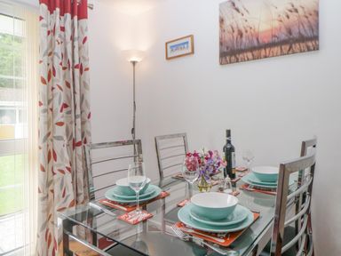 A dining area with a glass table set for four with plates bowls wine glasses and cutlery near a window with patterned curtains at Sycamores Rosecraddoc Lodge near Liskeard