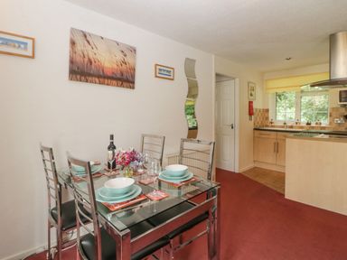 A dining area with a glass table set for four near a kitchen with light wood cabinets and a window at Sycamores Rosecraddoc Lodge near Liskeard