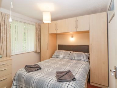 A bedroom with a bed flanked by built-in wardrobes and a window with curtains at Sycamores Rosecraddoc Lodge near Liskeard