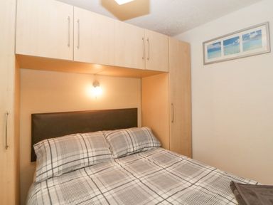 A bedroom with a bed under built in cabinets and a framed picture on the wall at Sycamores Rosecraddoc Lodge near Liskeard
