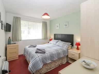A bedroom with a bed between two nightstands lamps and a window with curtains at Sycamores Rosecraddoc Lodge near Liskeard