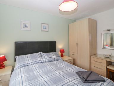 A bedroom with a double bed plaid bedding bedside tables with red lamps wardrobe and dressing table at Sycamores Rosecraddoc Lodge near Liskeard