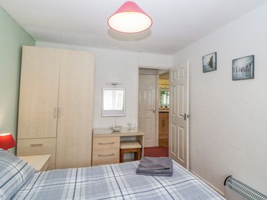 A bedroom with a bed, wardrobe, desk with a stool, a mirror, two framed pictures on the wall and a door open to another room at Sycamores Rosecraddoc Lodge near Liskeard