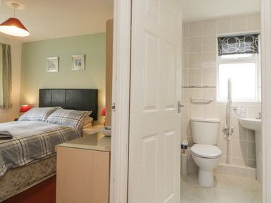 A bedroom with a bed and bedside tables next to a bathroom with a toilet and sink at Sycamores Rosecraddoc Lodge near Liskeard