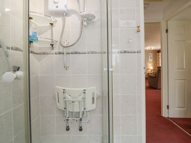 A tiled shower with a foldable seat and handheld showerhead at Sycamores Rosecraddoc Lodge near Liskeard