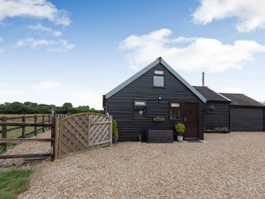 A black wooden single-story building with a gravel driveway and wooden gate at The Nook in Louth