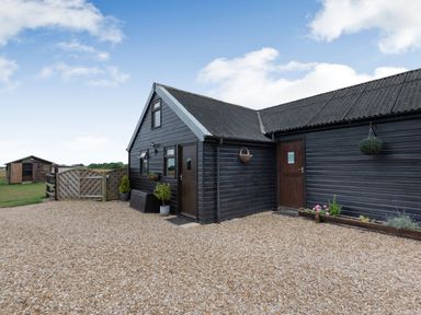 A black wooden building with two doors and windows surrounded by gravel and plants at The Nook in Louth