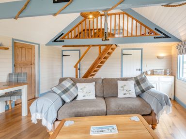 A living room with a sofa, wooden staircase, wooden doors, and a table at The Nook in Louth