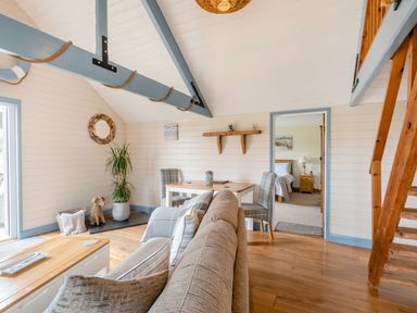 A living room with a beige sofa a dining table with two chairs a potted plant and wooden stairs at The Nook in Louth