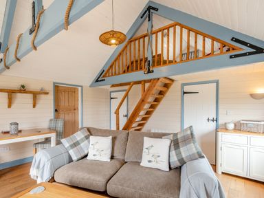 A living room with a beige sofa and wooden stairs leading to a loft at The Nook in Louth