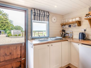 A kitchen with a wooden countertop a sink a kettle mugs on a shelf and a door opening outside at The Nook in Louth