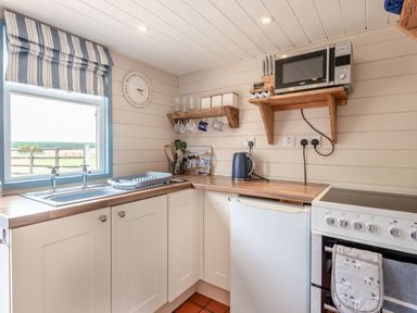 A kitchen with a window above the sink a microwave kettle stove and wooden shelves at The Nook in Louth