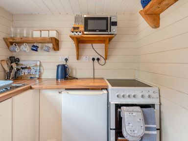 A kitchen corner with a microwave on a wooden shelf kettle stove and hanging mugs at The Nook in Louth