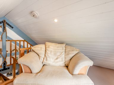 A beige armchair with cushions under a sloped white ceiling near wooden railing at The Nook in Louth