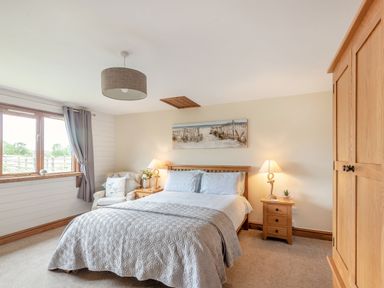 A bedroom with a bed two bedside tables with lamps an armchair a window with curtains and a wooden wardrobe at The Nook in Louth