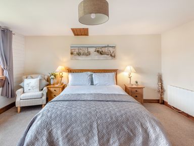 A bedroom with a bed and two bedside tables with lamps an armchair with cushions and a painting above the bed at The Nook in Louth