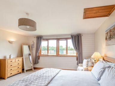 A bedroom with a bed bedside table lamp wooden dresser standing mirror window with curtains and a chair at The Nook in Louth