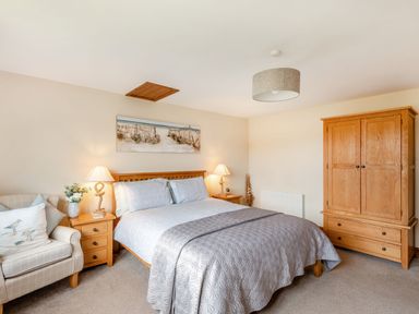 A bedroom with a double bed flanked by two lamps on wooden bedside tables a wooden wardrobe and an armchair with cushions at The Nook in Louth