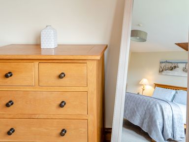 A wooden dresser with a patterned vase on top and a mirror reflecting a bedroom with a bed lamp and painting at The Nook in Louth