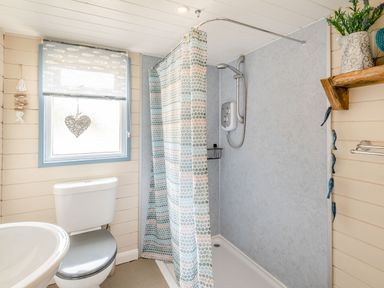 A bathroom with a shower area curtain toilet and a window with a heart decoration at The Nook in Louth