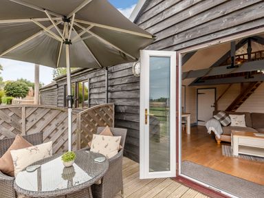 An outdoor seating area with a glass table umbrella and chairs next to an open door leading to a living room at The Nook in Louth
