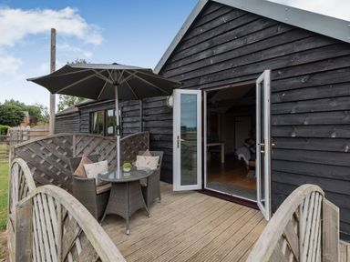 An outdoor wooden deck with a table with chairs and an umbrella next to a black wooden building at The Nook in Louth
