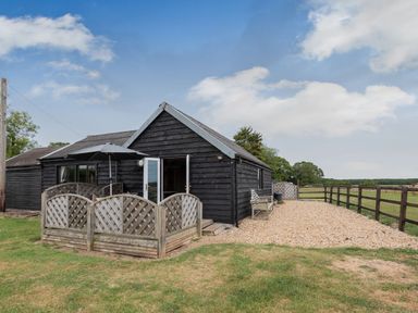 A black wooden barn with a patio area and umbrella beside a fenced gravel yard at The Nook in Louth