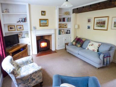 A living room with armchairs a sofa a wood burning stove and bookshelves at Woodside Cottage in Brompton-by-Sawdon