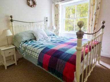 A bedroom with a metal bed frame bedside table and lamp near a window at Woodside Cottage in Brompton-by-Sawdon