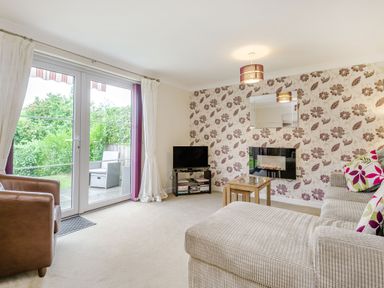 A living room with a sofa a brown armchair a small table a television and glass doors leading outside at Kymin View in Monmouth