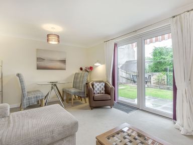 A living room with a glass table and chairs a leather armchair and large windows overlooking a garden at Kymin View in Monmouth