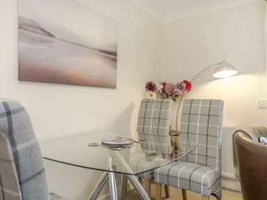 A glass dining table with three checkered chairs a vase of flowers and a wall lamp at Kymin View in Monmouth