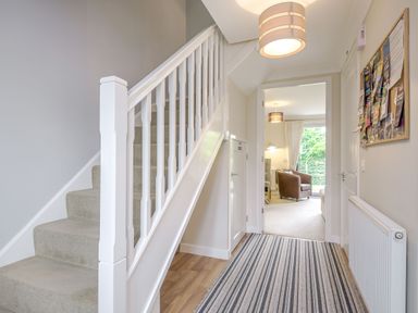 A hallway with a striped rug leading to a sitting room with armchairs at Kymin View in Monmouth