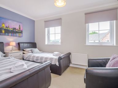 A bedroom with two single beds a nightstand a lamp an armchair two windows and a wall painting at Kymin View in Monmouth