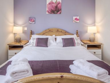 A bedroom with a wooden double bed two bedside tables with lamps folded towels on the bed and floral pictures on the wall at Kymin View in Monmouth