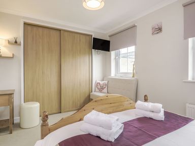 A bedroom with a wooden bed folded towels a sofa with a heart pillow a TV and wooden closet doors at Kymin View in Monmouth