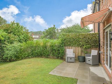 A backyard with grass a paved patio two chairs a potted plant and a striped awning at Kymin View in Monmouth