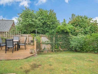 A backyard with a wooden deck and outdoor table and chairs next to a wooden fence covered in ivy at Kymin View in Monmouth