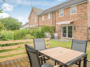 A backyard with a wooden deck and patio furniture next to a brick house with glass doors at Kymin View in Monmouth