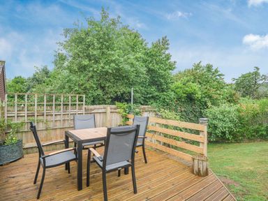 An outdoor wooden deck with a table and four chairs surrounded by wooden fences and green bushes at Kymin View in Monmouth