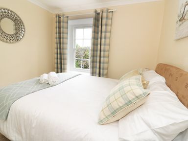 A bedroom with a bed made with white linens and plaid pillows near a window with plaid curtains at Dolau Farmhouse in Lampeter