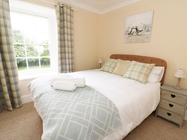 A bedroom with a bed with pillows and towels near a window with curtains and bedside tables at Dolau Farmhouse in Lampeter